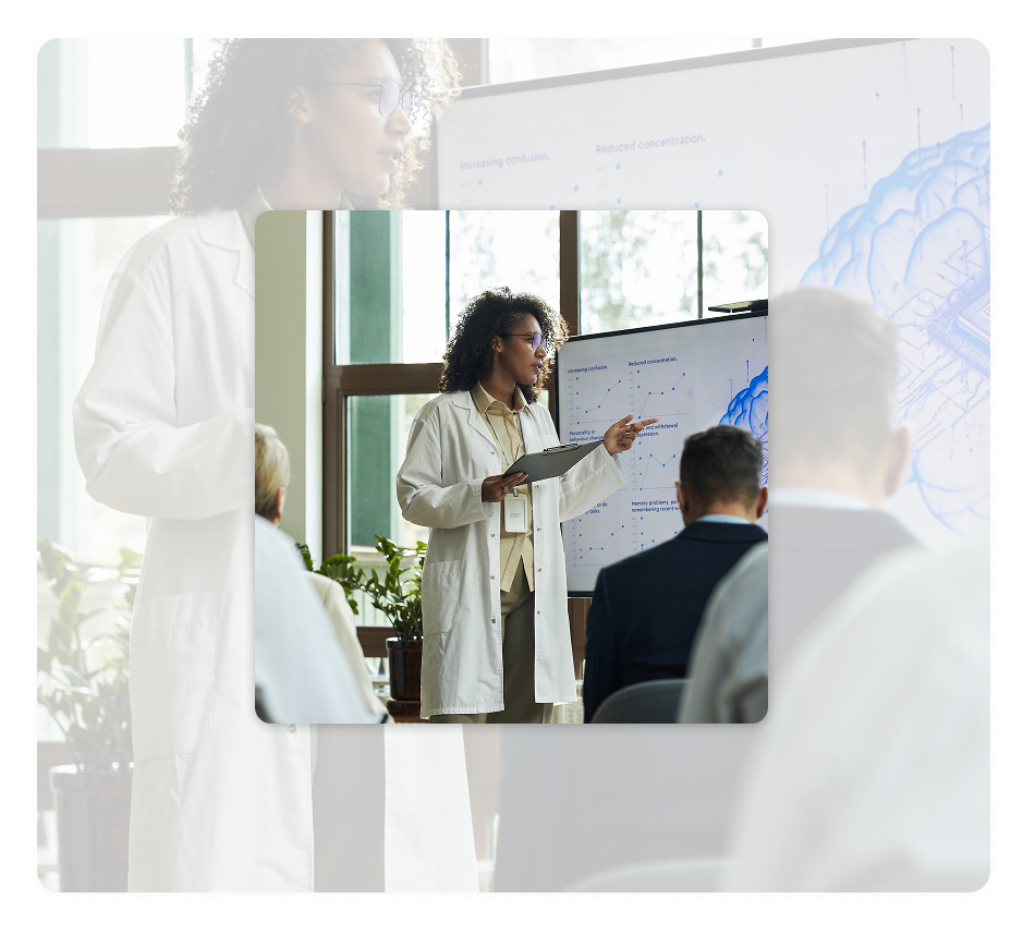 Three healthcare professionals in white coats discussing around a conference table with a laptop, on a white gradient background